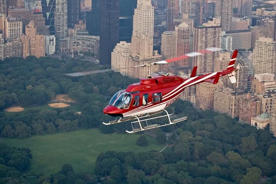 A red helicopter is flying over Central Park with the New York City skyline in the background.