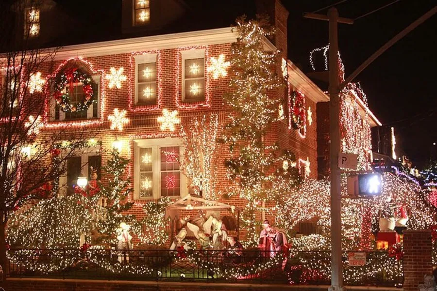 The image shows a brick house elaborately decorated with numerous Christmas lights and festive decorations, including a nativity scene.