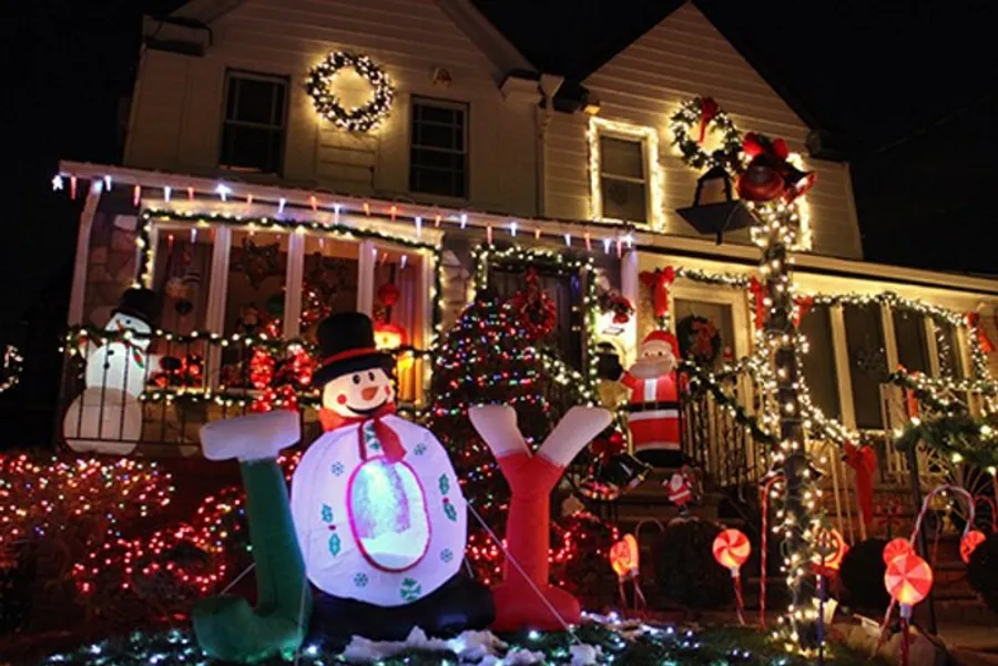 A house is festively decorated with colorful lights, inflatable holiday figures, wreaths, and a Christmas tree, creating a vibrant and cheerful nighttime display for the holiday season.