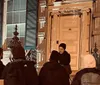 A group of people is sitting and standing on a city sidewalk at night engaging in conversation near a building labeled THE COOPER UNION