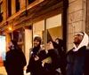 A group of people is sitting and standing on a city sidewalk at night engaging in conversation near a building labeled THE COOPER UNION