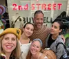 Five people are posing for a selfie with smiles in front of a store called 2nd STREET with colorful graffiti-like art on the windows behind them
