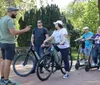 Four individuals are standing in a park-like setting with the person on the left appearing to speak and gesture to the others who are attentively listening