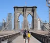 Pedestrians walk across the Brooklyn Bridge with its distinctive Gothic arches against the backdrop of the New York City skyline on a clear day