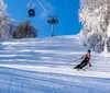 Two skiers are descending a snowy slope with a ski lift operating in the background under a clear blue sky