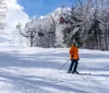 Two skiers are descending a snowy slope with a ski lift operating in the background under a clear blue sky