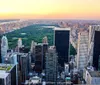 A coin-operated binocular viewer stands on an observation deck with a clear view of a city skyline featuring a prominent skyscraper under a blue sky