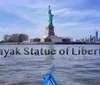 The image shows the view from a kayak on the water near the Statue of Liberty with the New York City skyline in the background