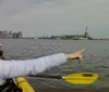 The image shows the view from a kayak on the water near the Statue of Liberty with the New York City skyline in the background