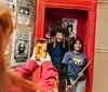 A person is taking a photo of two smiling individuals posed playfully in a red telephone booth decorated with Harry Potter themed posters