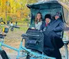 Three people are smiling while sitting in a pedicab in a park with autumn foliage in the background