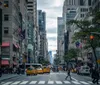 A bustling city street is depicted with pedestrians crossing vehicles including yellow cabs and lined with tall buildings and American flags fluttering in the breeze