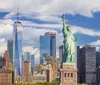 The image features the Statue of Liberty in the foreground with the New York City skyline including One World Trade Center in the background under a partly cloudy sky