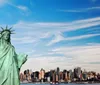 The image features the Statue of Liberty in the foreground with the New York City skyline including One World Trade Center in the background under a partly cloudy sky