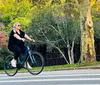 A person is biking along a street with lush greenery and colorful trees in the background