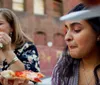 Two people are smiling and holding up large slices of pizza to their mouths as if taking a bite in a casual dining setting