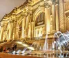 The image shows an illuminated classical building at night with a grand staircase and an elegant fountain in the foreground likely a museum or a similar cultural institution