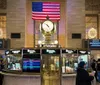 The photo shows the bustling interior of Grand Central Terminal with people milling about under the expansive arched windows and a large American flag hanging prominently