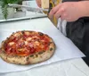 The image shows a freshly baked pizza with a golden-brown crust and melted cheese speckled with charred spots typical of a wood-fired oven