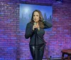 A person is performing stand-up comedy on a stage with a brick wall background and a cityscape sign