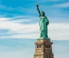 The Statue of Liberty stands tall against a blue sky with wispy clouds