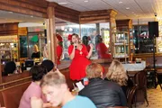 A person in a red dress is performing or speaking into a microphone in front of an audience at an indoor venue.