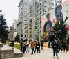 People stroll by a modern building with an artistic mural near a Christmas tree in an urban park setting