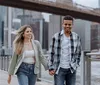 A joyful couple is engaging in a piggyback ride with the woman on the mans back both smiling towards the camera with city buildings and trees in the background