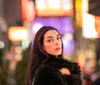 A joyful woman is playfully flipping her hair in a bustling city street illuminated by vibrant neon signs at dusk