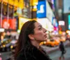 A joyful woman is playfully flipping her hair in a bustling city street illuminated by vibrant neon signs at dusk