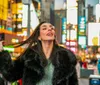 A joyful woman is playfully flipping her hair in a bustling city street illuminated by vibrant neon signs at dusk