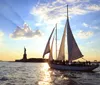 A sailboat is gliding across the water near the Statue of Liberty during a beautiful sunset