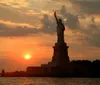 A sailboat is gliding across the water near the Statue of Liberty during a beautiful sunset