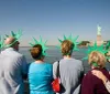 A group of tourists wearing green foam Statue of Liberty crowns gazes at the real Statue of Liberty from a boat