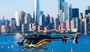 A helicopter is flying over a body of water with a dense urban skyline in the background.