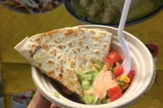 A person is holding a plate with a quesadilla and toppings of guacamole, salsa, and a spoonful of cream or cheese.