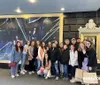 A group of smiling people are posing for a photo in front of a large promotional poster for a theatrical performance