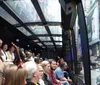 The image captures a group of people on a transparent-roofed sightseeing bus tour enjoying the cityscape with one person enthusiastically pointing out a feature