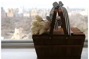 A wooden basket with white roses and a striped ribbon sits on a windowsill with a blurred cityscape in the background.
