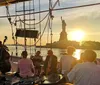 A group of people is enjoying a live music performance on a boat at sunset with the Statue of Liberty in the background