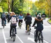 A group of people are cycling along a tree-lined road in what appears to be an urban park setting with autumn foliage