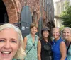 A group of five smiling women takes a selfie together in front of a historic brick building with an arched metal door