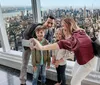 A family is taking a selfie with a smartphone inside a high-rise building overlooking a panoramic cityscape