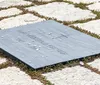 This image displays a grave marker inscribed with the name John Fitzgerald Kennedy and the years 1917 - 1963 adorned with several coins placed on top