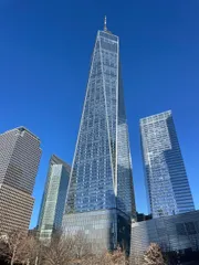 This image shows a tall, striking skyscraper dominating the skyline against a clear blue sky, surrounded by several other high-rise buildings.