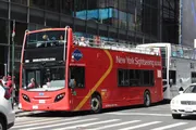A red double-decker sightseeing tour bus is navigating through a busy urban street.