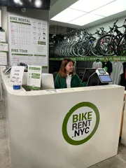A person is seated behind the counter of a bike rental shop, with information on bike rentals and tours visible in the background.