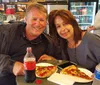 A smiling man and woman are enjoying slices of pizza and soft drinks while sitting at a table