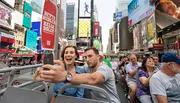 A couple is excitedly taking a selfie on a sightseeing bus in the bustling atmosphere of Times Square.