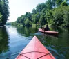 Two people are kayaking on a calm river surrounded by lush greenery on a sunny day